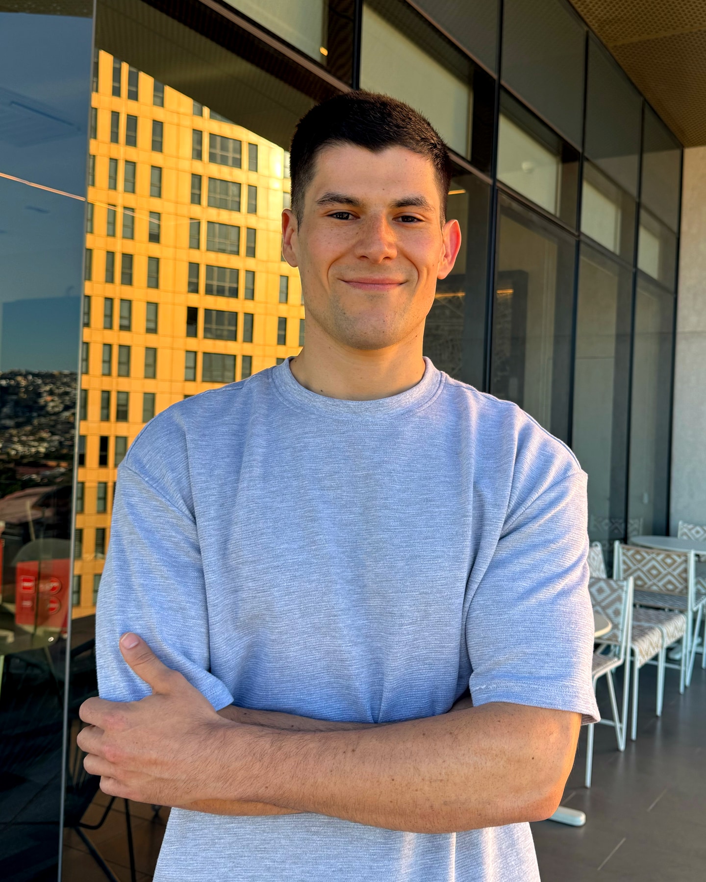 Ruben smiling with his arms crossed on a city terrace at golden hour, sunlit buildings behind him